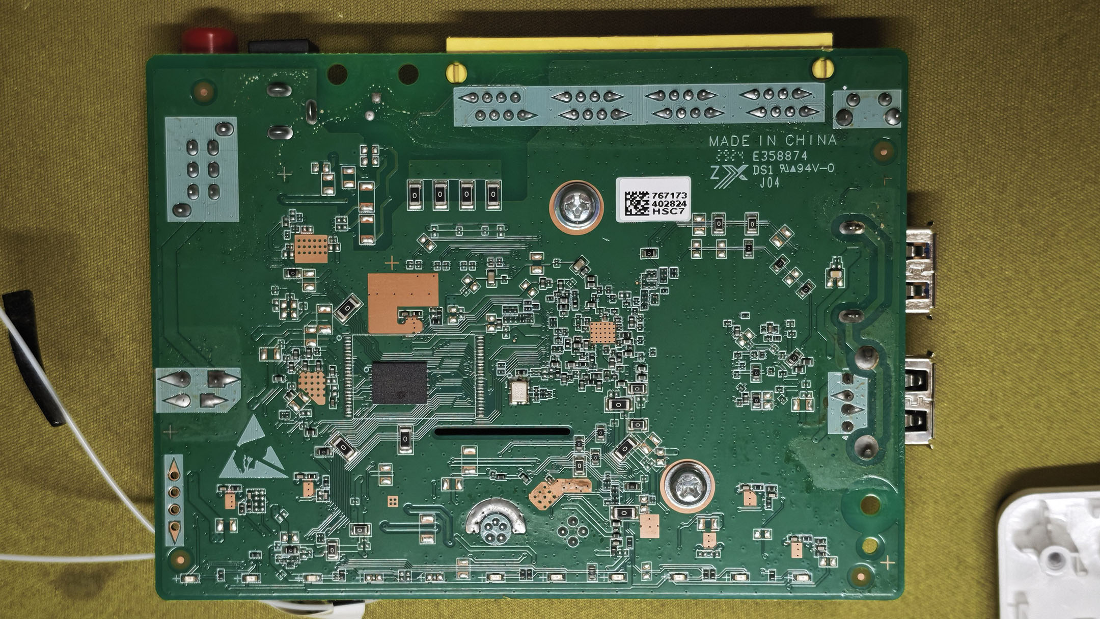 中国移动 F7005MV3 主板这一面:中间一颗方形闪存芯片,周围有密集焊盘,板上丝印 MADE IN CHINA、E358874、94V-0,右侧是四个 RJ45 网口的针脚和一个条码贴纸