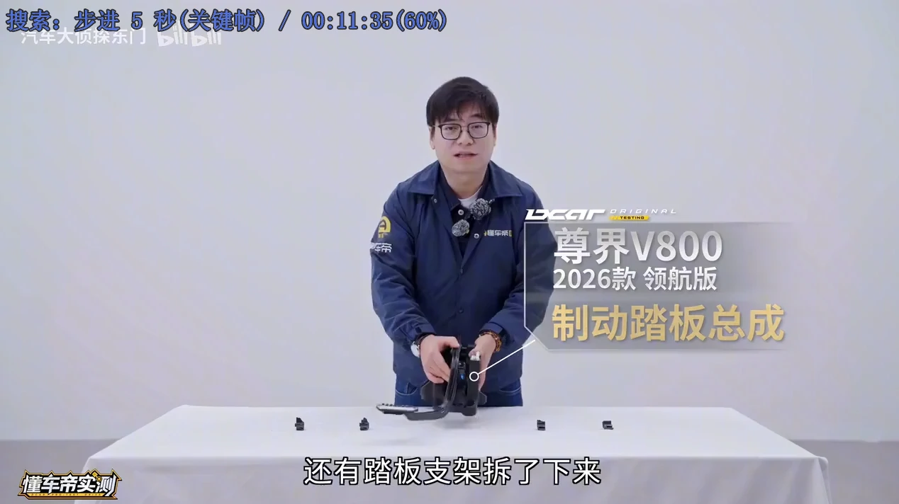 测试人员手持拆下来的尊界V800 2026款领航版制动踏板总成,桌面上摆着散落的断裂碎片